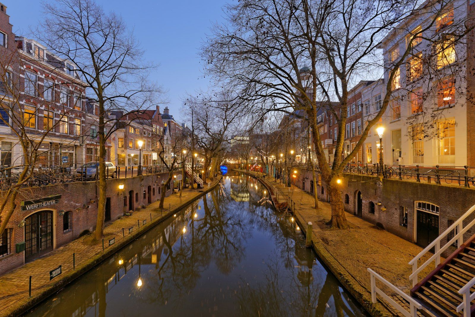 Utrecht canal at dusk with lit windows and bare trees reflected in the water