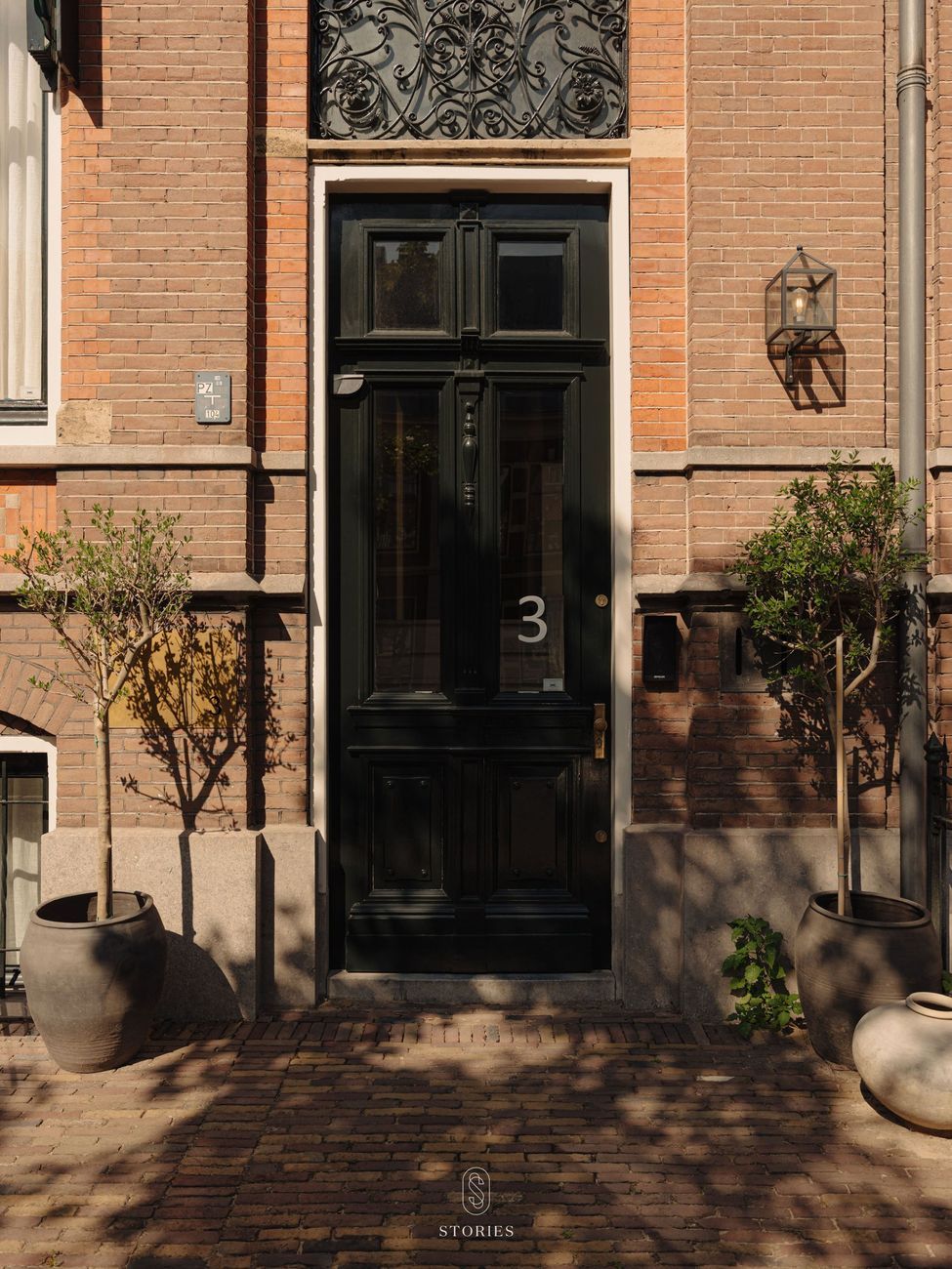 The black front door of number 3 between two small olive trees in terracotta pots