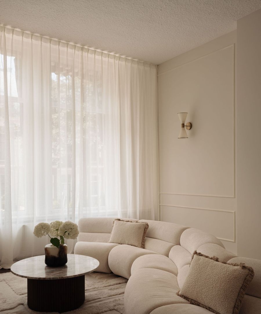 The waiting room at Stories, with a curved cream sofa, white hydrangeas on a round table and sheer curtains at the window